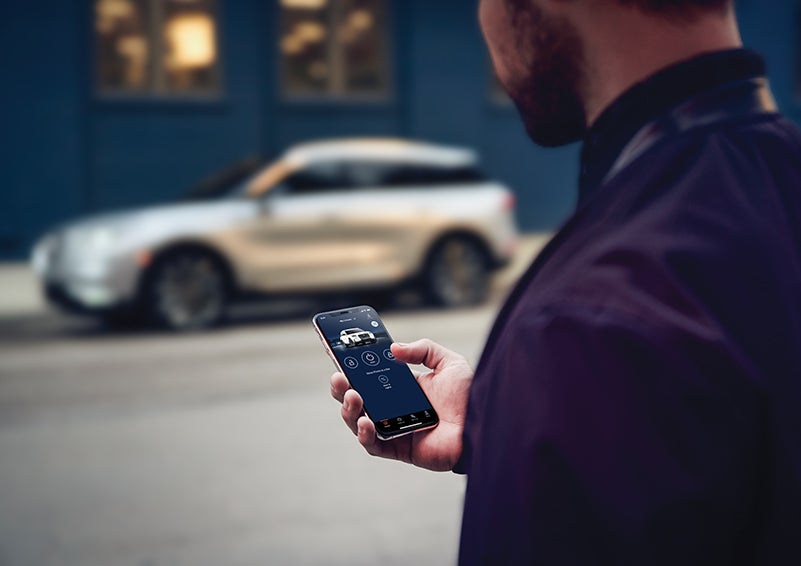 A person is shown interacting with a smartphone to connect to a Lincoln vehicle across the street. | West Point Lincoln of Sugar Land in Houston TX